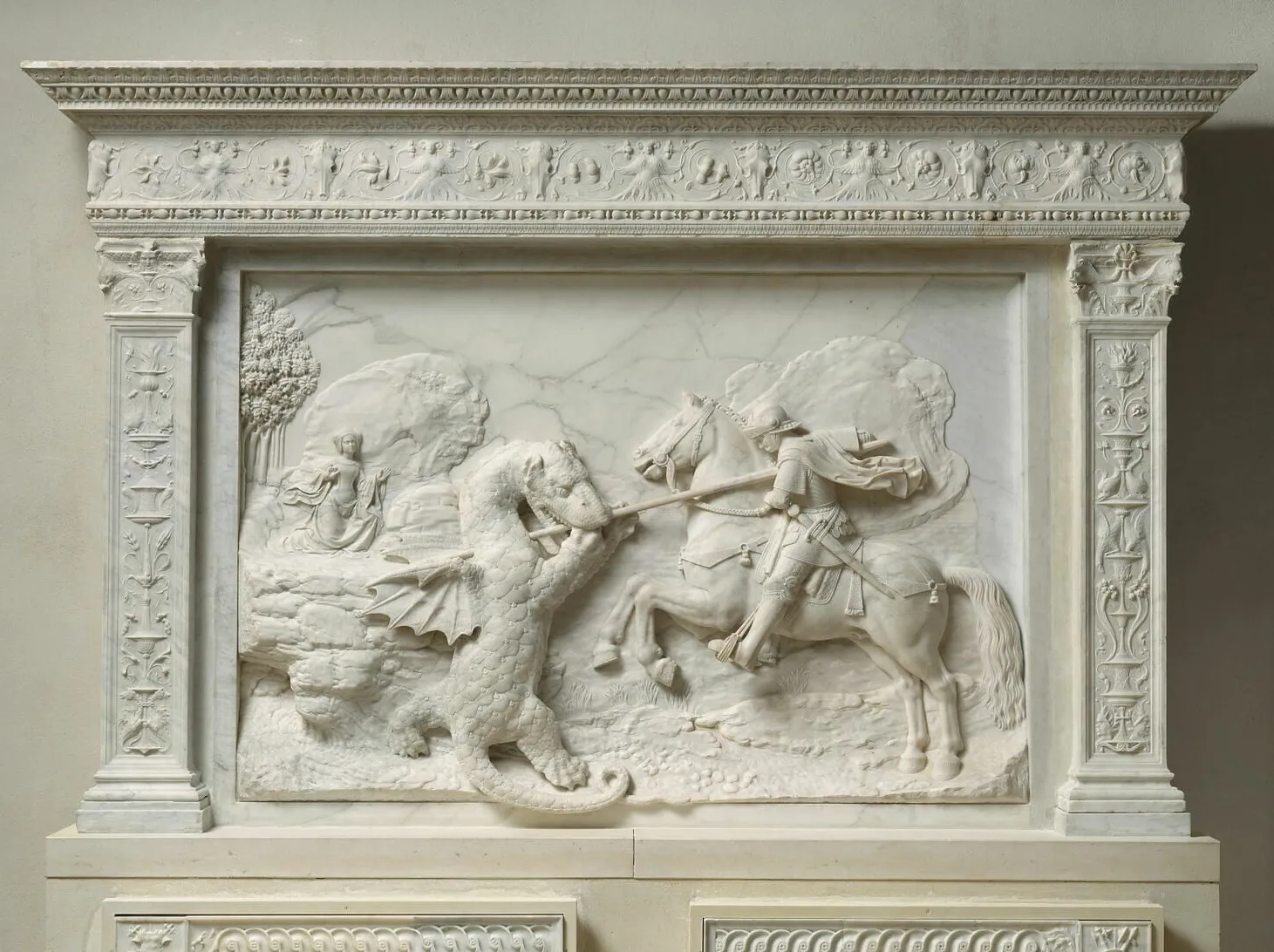 L'image est la photographie d'un bas-relief en marbre représentant le combat d'un cavalier (à droite) et d'un dragon (à gauche). On apperçoit au second plan, à gauche, une jeune femme qui observe la scène.