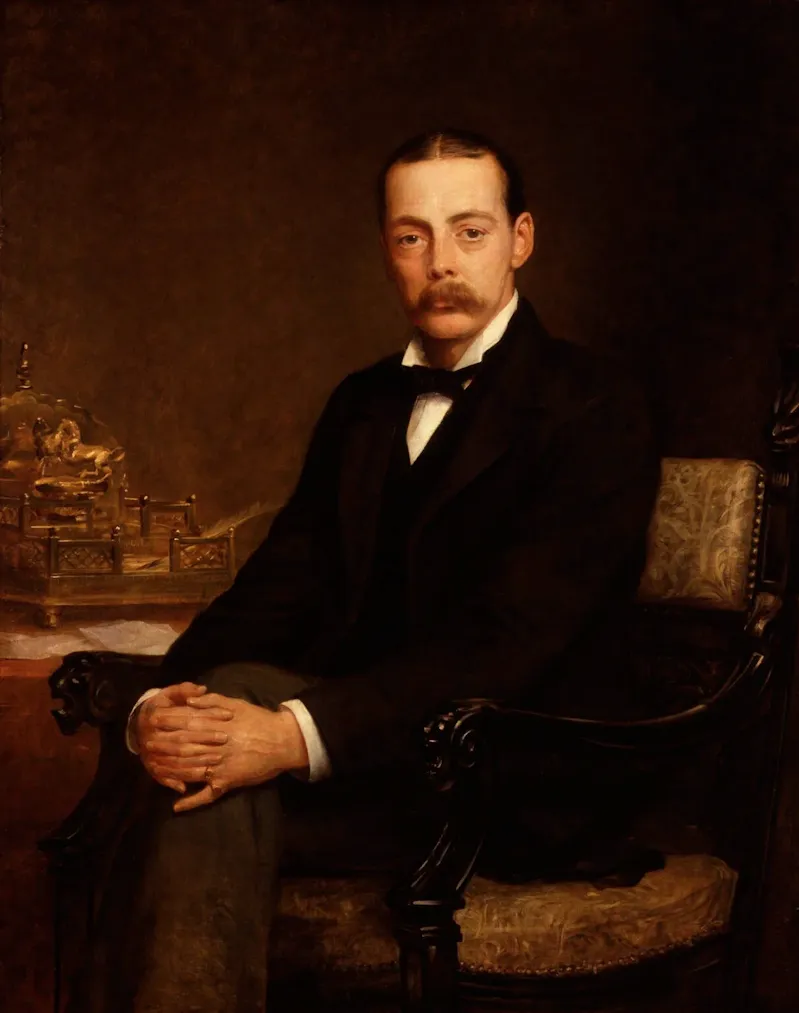 Portrait de Lord Randolph Churchill. Un jeune homme moustachu en costume est assis dans un fauteuil et nous regarde, les jambes croisées et les mains jointes sur son genou droit. Derrière lui on apperçoit une table avec des papiers et un écritoire.