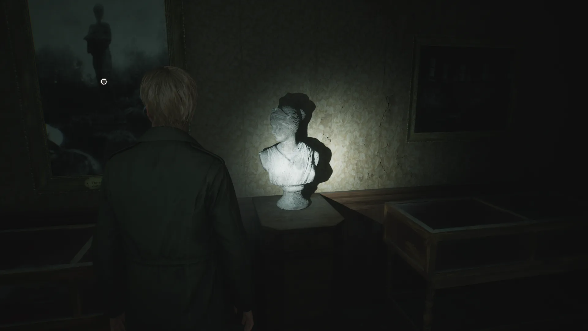 Capture d'écran de Silent Hill 2 qui montre le personnage de James Sunderland de dos. Il se trouve dans une petite salle d'exposition et il fait face à un petit piédestal sur lequel est posé un buste qui reprend le modèle de la sculpture antique dite "Diane de Versailles"