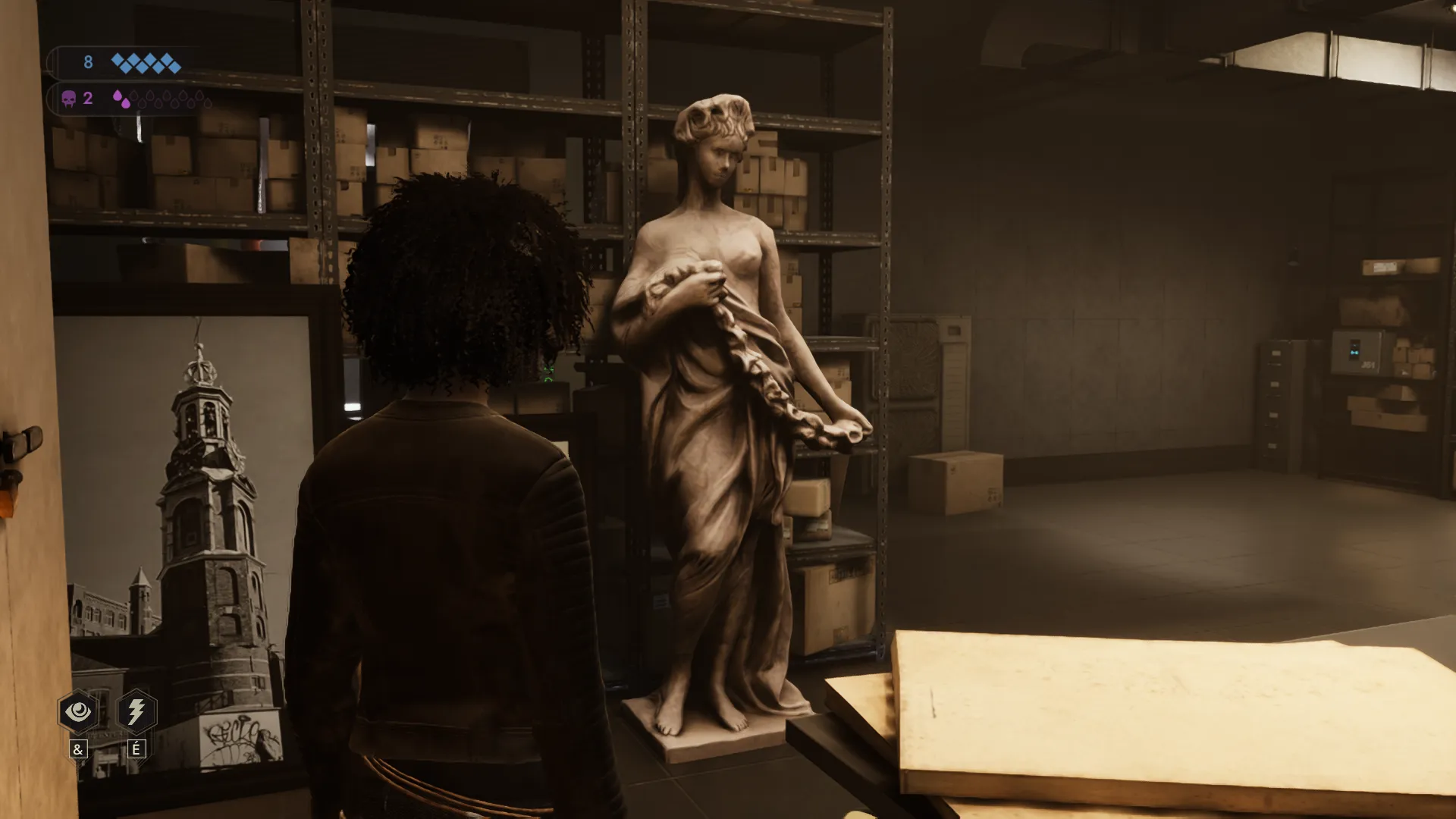L'image est une capture d'écran du jeu vidéo Vampire: The Masquerade – Swansong. On y voit le personnage joueur de dos, debout dans ce qui semble être un entrpôt ou une zone de stockage, avec des étagères en métal supportant des alignements de cartons. Contre une de ces étagères, face au personnage joueur, se trouve une statue en pierre ou en marbre d'environ 2m représentant une jeune femme
