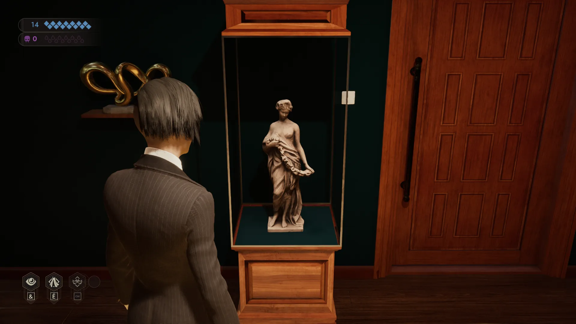 L'image est une capture d'écran du jeu vidéo Vampire: The Masquerade – Swansong. On y voit le personnage joueur de dos, debout dans une pièce aux murs couleur vert sapin. Face au personnage joueur, contre le mur, une vitrine jouxte une porte en bois claire. La vitrine renferme une statuette représentant une jeune femme.